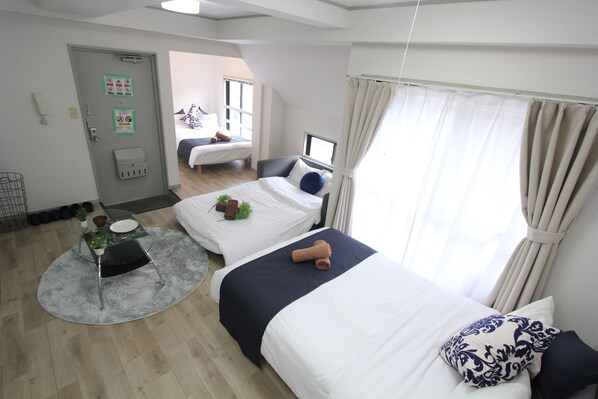 A hotel room with two beds, a small table with a plant, a window with curtains, and a door with signs.