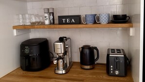 Et køkken med lyse skabe, kaffemaskine, brødrister og en thekasse på bordpladen.