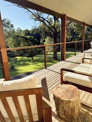 Una terraza de madera con asientos al aire libre, un tocón de árbol y vistas a un área verde con árboles.
