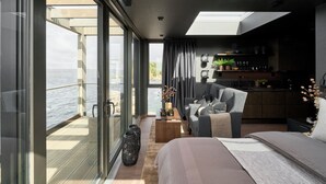 A modern bedroom with a large window, a sofa, a bed, and a small kitchen area. - Hideaway Herdla 1 – unique and luxurious cabin 15 m above the sea near Bergen (Herdla)