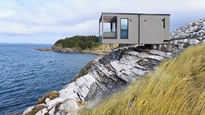 A modern cabin-style building with a large window, situated on a rocky cliff overlooking the sea. - Hideaway Herdla 1 – unique and luxurious cabin 15 m above the sea near Bergen (Herdla)
