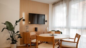 A modern living room with a round wooden table, four chairs, a television mounted on a wooden panel wall, and a potted plant. - Apartment 'Riversidesuite Tübingen' with Shared Terrace, Shared Garden and Wi-Fi (Tübingen)