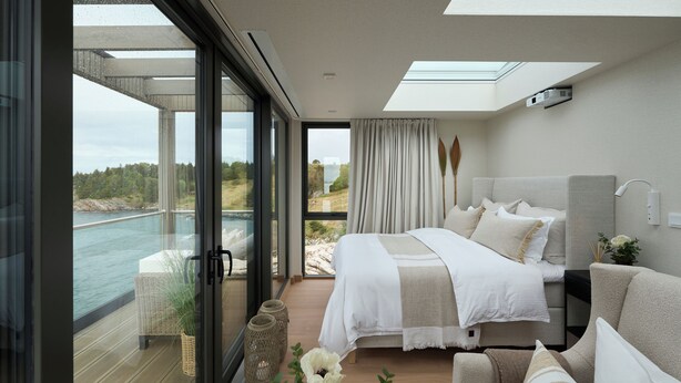 Une chambre moderne avec un grand lit, un canapé et une vue sur la mer grâce à de grandes fenêtres du sol au plafond.