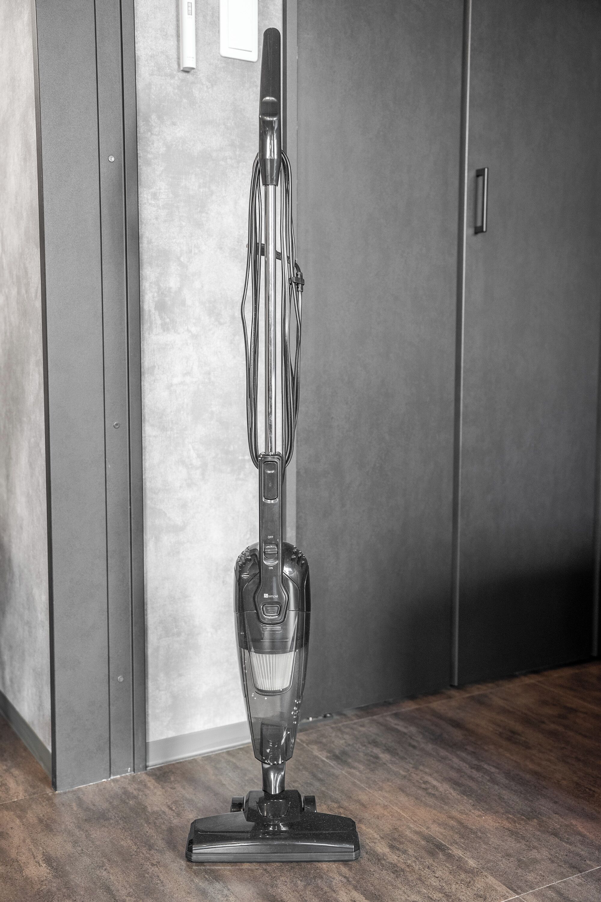 A vacuum cleaner on a wooden floor in a room with a concrete wall and a door.