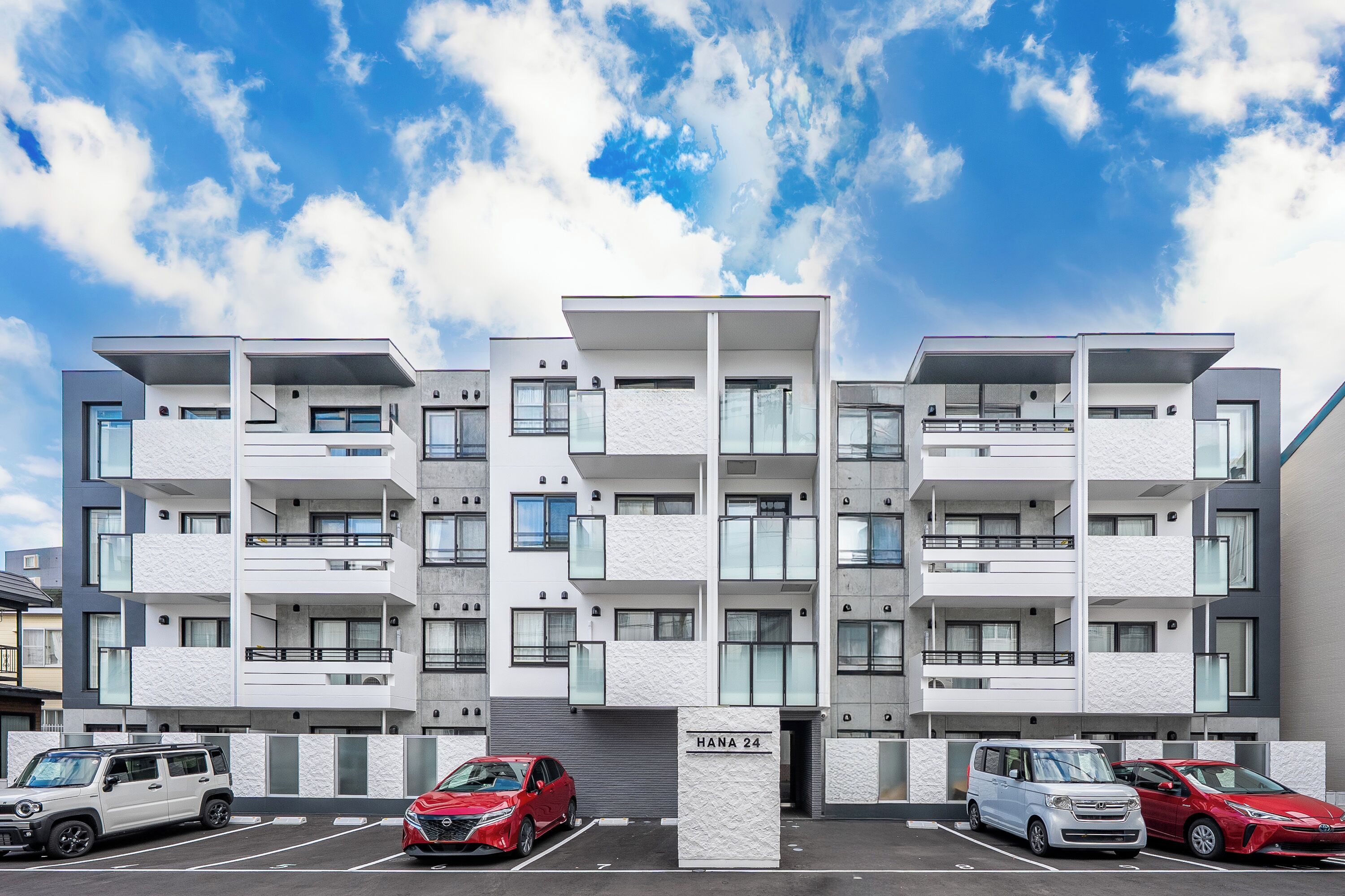 A modern apartment building with multiple balconies and a parking area.
