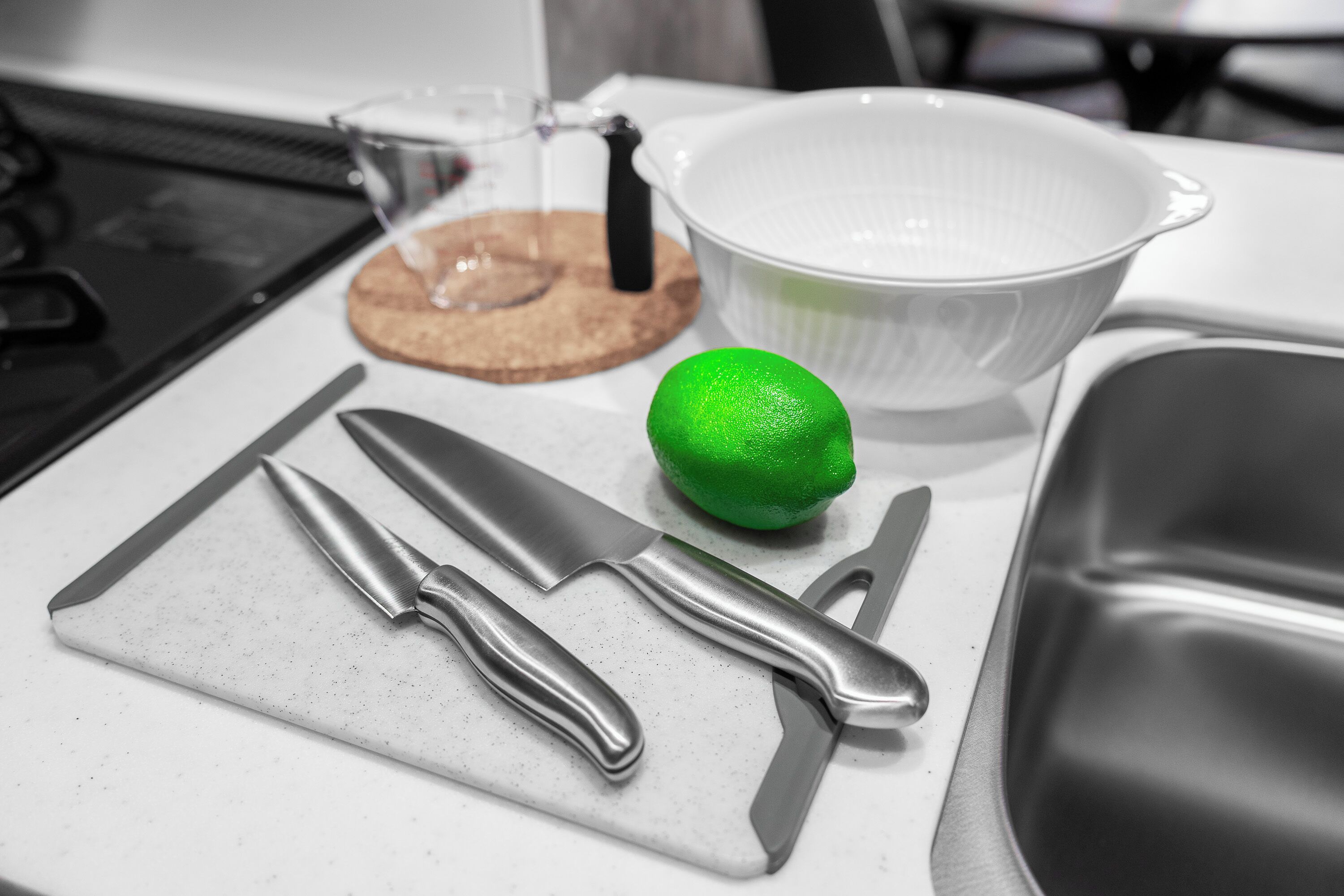 A kitchen counter with a cutting board, two knives, a lemon, a glass container, and a white bowl.