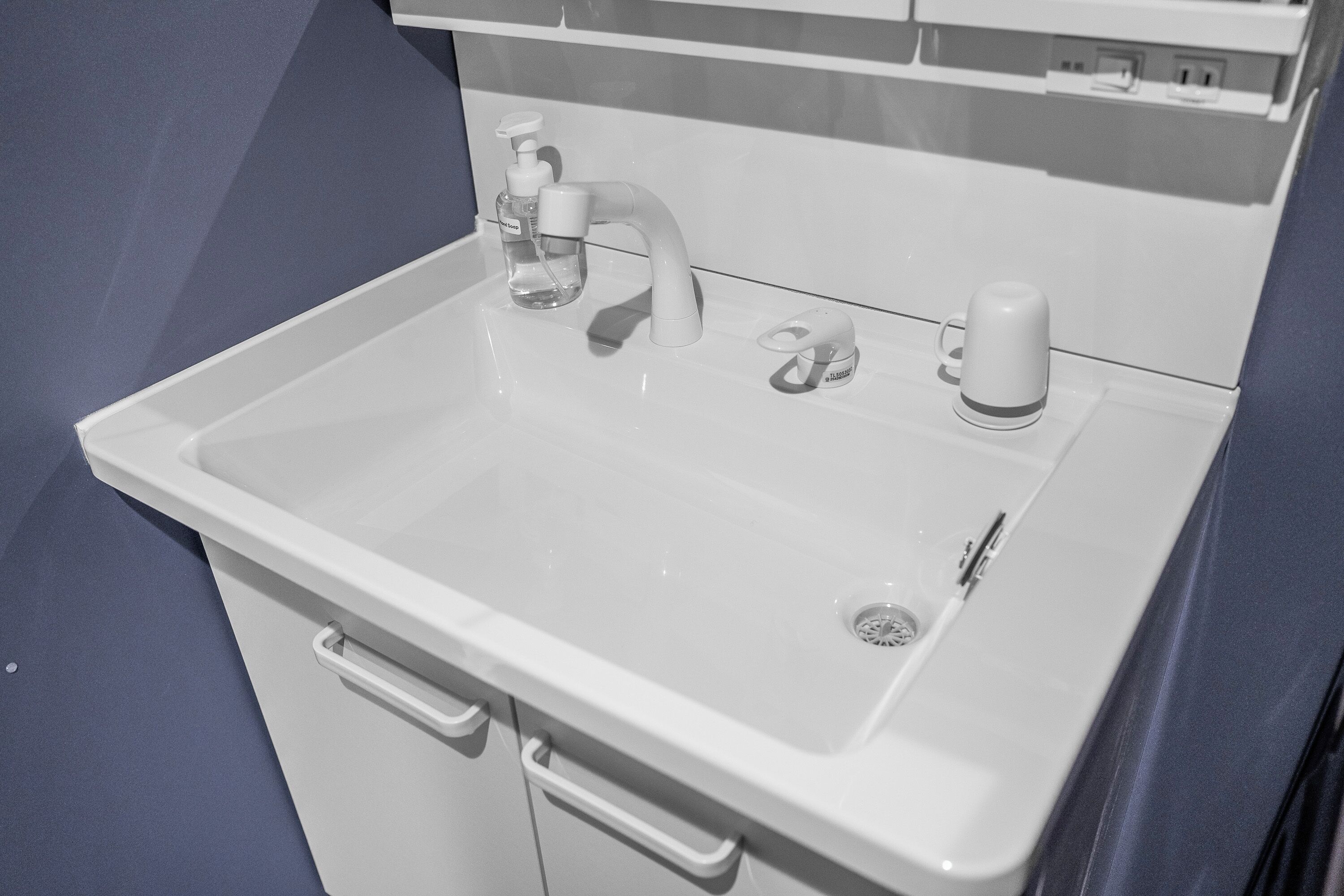 A white bathroom sink with a faucet, soap dispenser, and cup holder.