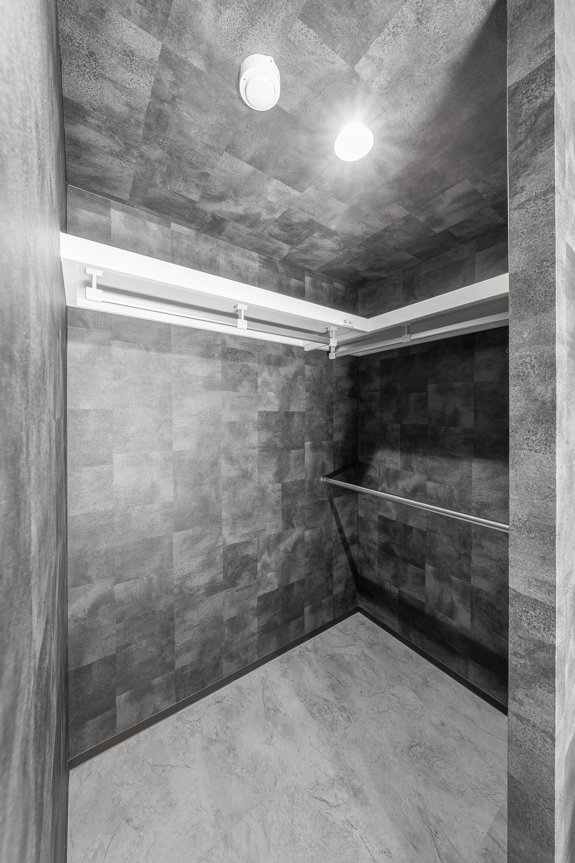 A modern shower area with a tiled wall and ceiling, a metal handrail, and a ceiling light.