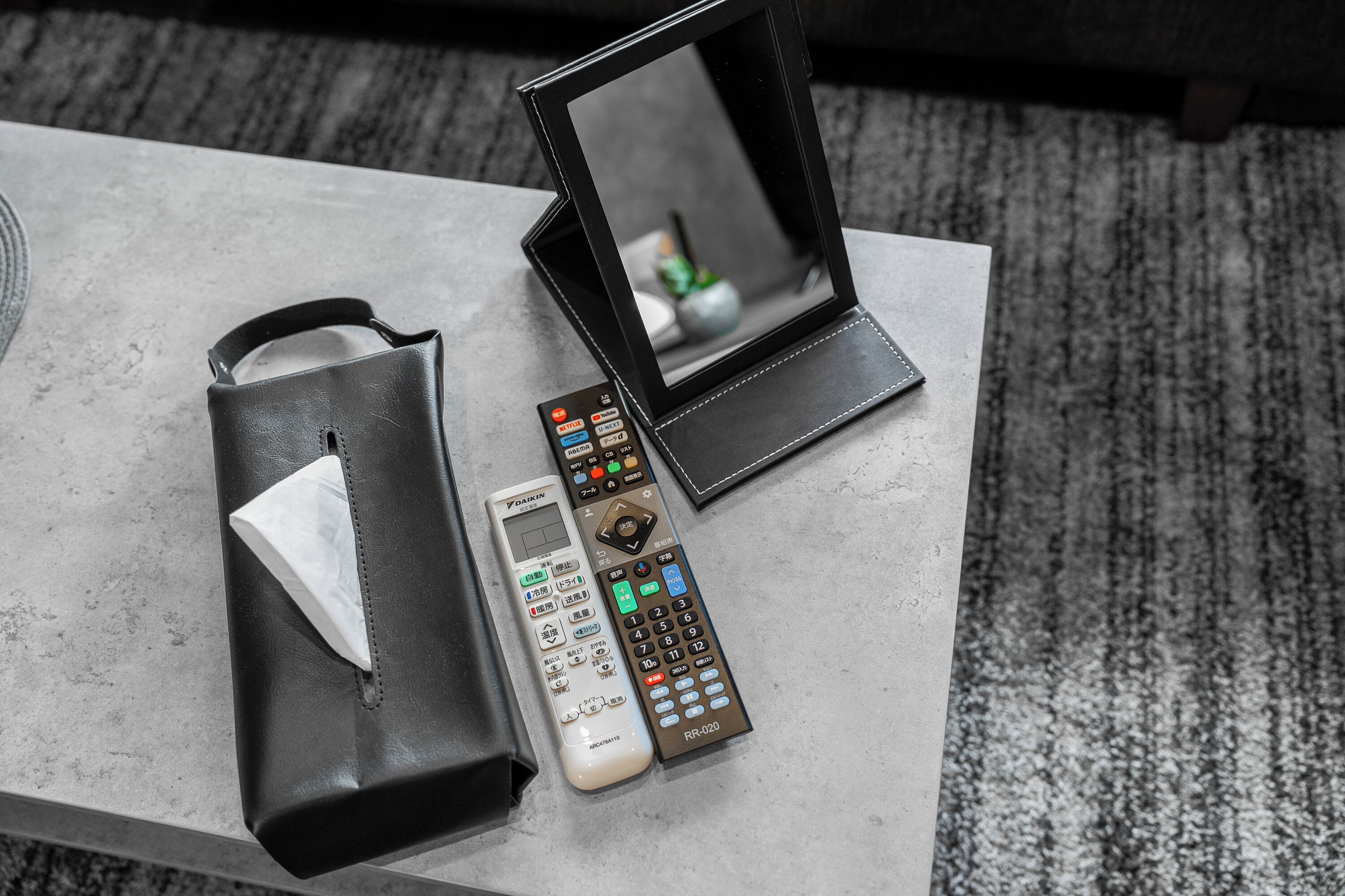 A remote control, a tissue, and a small mirror on a table.