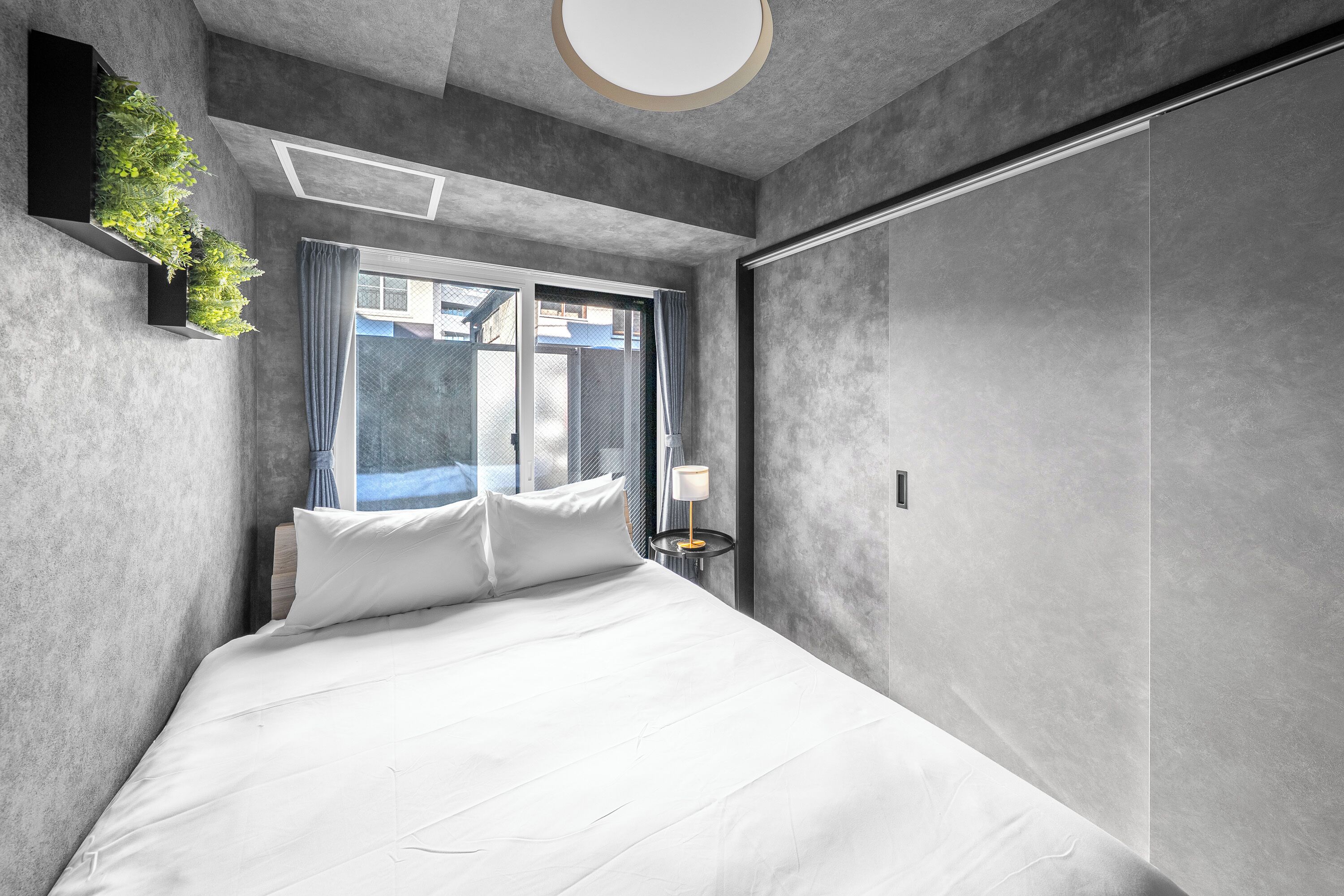 Een moderne hotelkamer met een groot bed, een nachtkastje met een lamp, een raam met gordijnen en een wandplant.