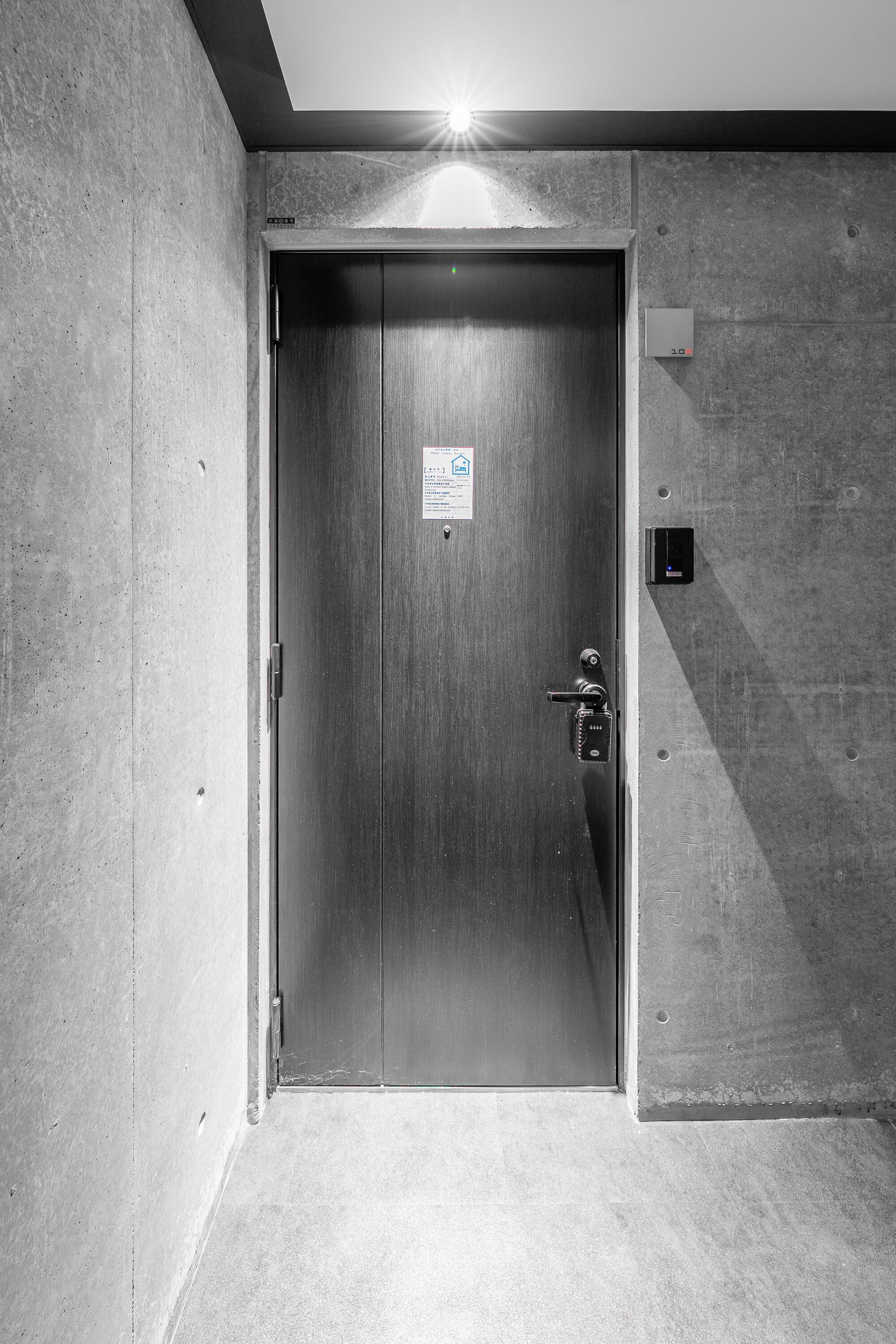 En metalisk elevatordør med et tastefeltlås, et lille skilt på væggen og en lampe over døren.