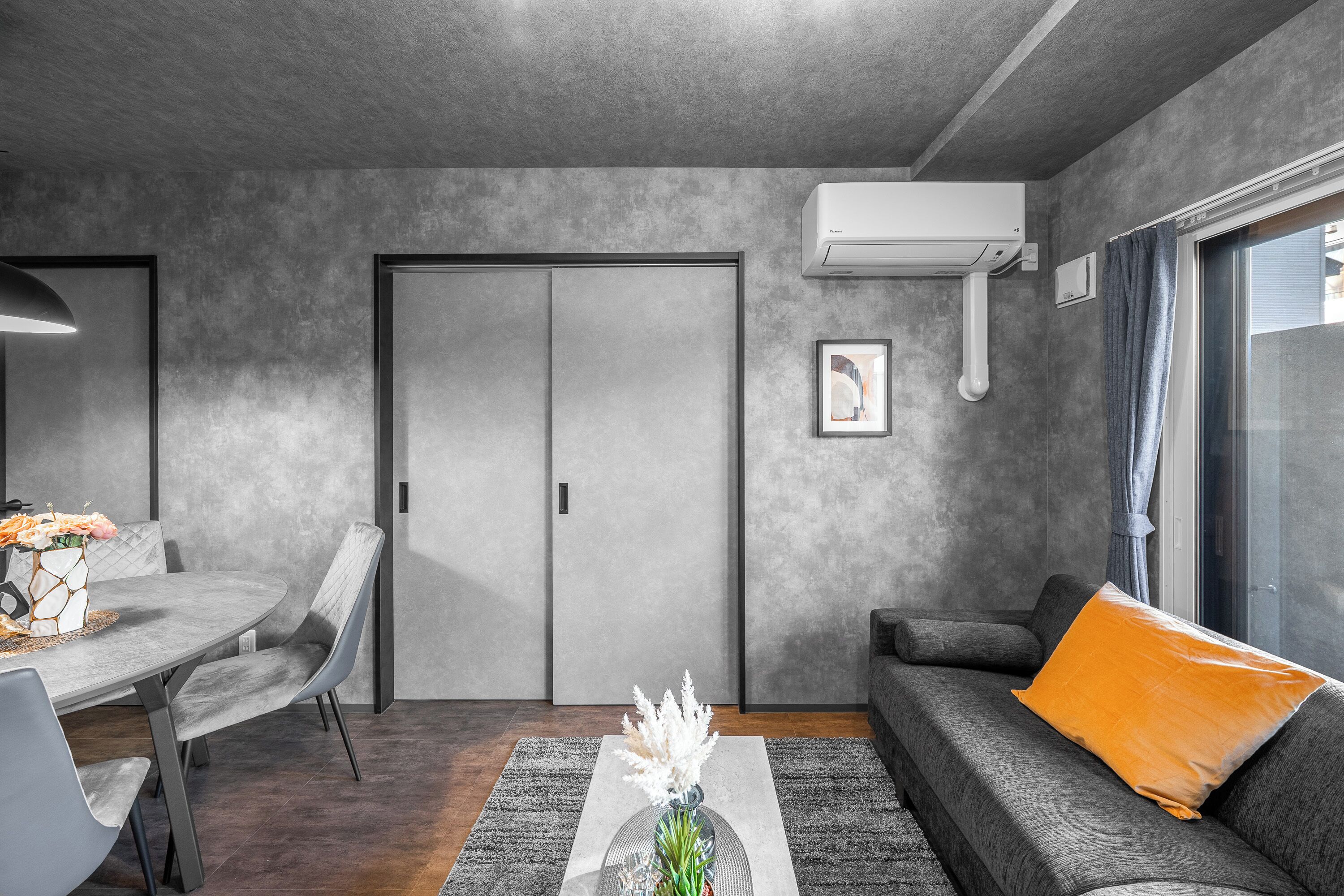 Ein modernes Wohnzimmer mit grauem Sofa, einem Esstisch mit Stühlen und einem grauen Teppich.