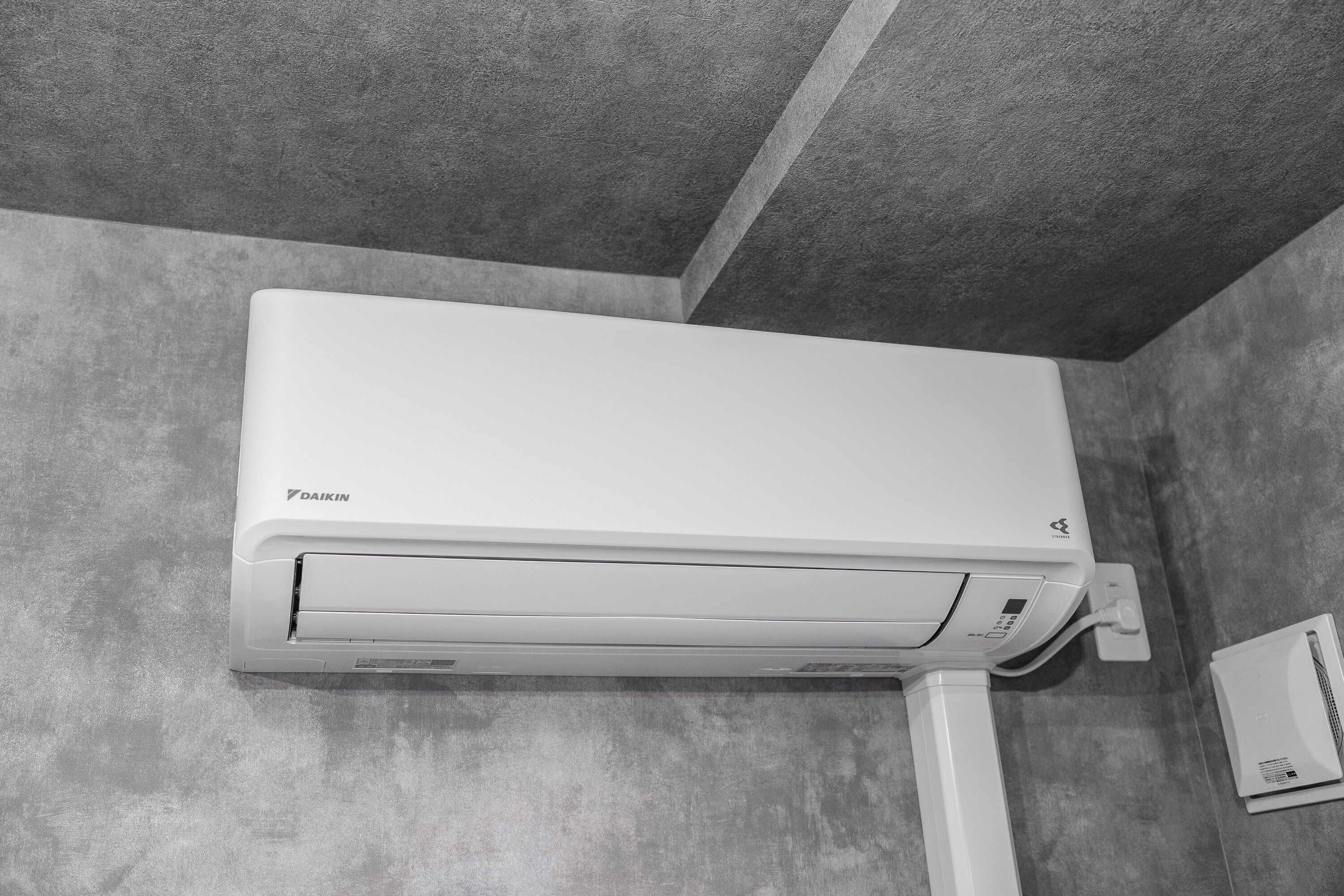A white Daikin air conditioner mounted on a grey textured wall.
