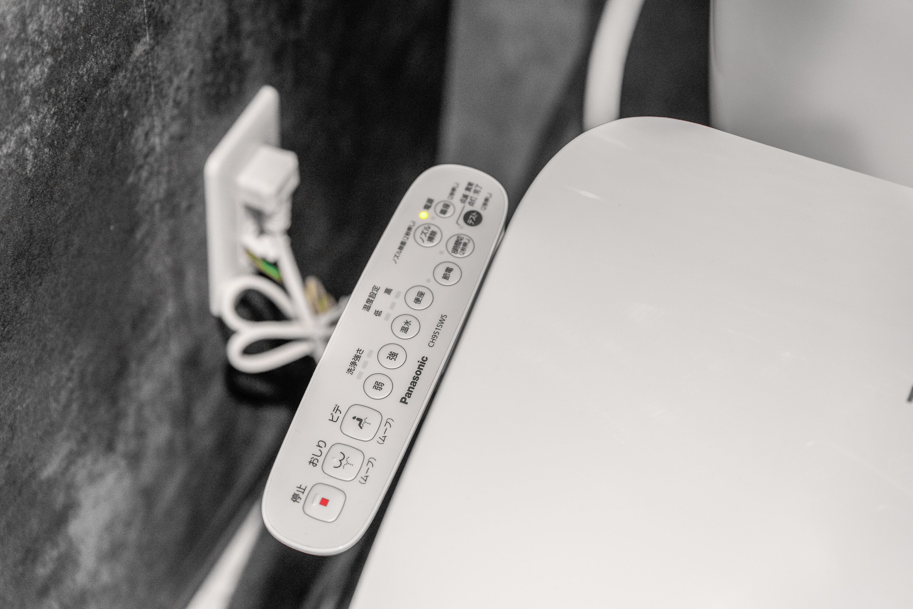 Un telecomando con scritte giapponesi, posizionato accanto a un elettrodomestico bianco, probabilmente un frigorifero.