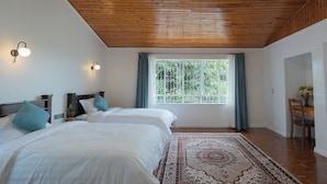 A bedroom with two beds, wooden ceiling, large window with curtains, and a patterned rug. - United House (Nairobi)