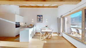 A modern kitchen with white cabinetry, a central island, and a dining area with a wooden table and chairs. - Charming holiday home in an excellent, quiet location in sun-drenched Pontresina (Pontresina)