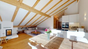 A spacious loft with exposed wooden beams, a living area with a sofa and coffee table, a kitchen with modern appliances, and a dining area with a wooden table and chairs. - Charming holiday home in an excellent, quiet location in sun-drenched Pontresina (Pontresina)