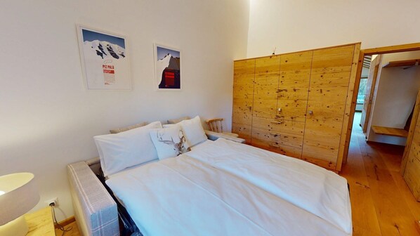 A bedroom with a bed, a wooden wardrobe, and two framed pictures on the wall. - Charming holiday home in an excellent, quiet location in sun-drenched Pontresina (Pontresina)