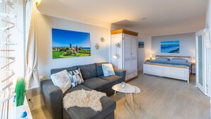 Een moderne woonkamer met een bank, een klein rond tafeltje en een bed met een houten hoofdeinde.