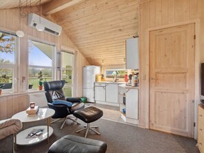 A cozy cabin interior with a dining area, a kitchen, and a seating space with a chair and ottoman. - 5 Star Holiday Home in Grindsted (Grindsted)