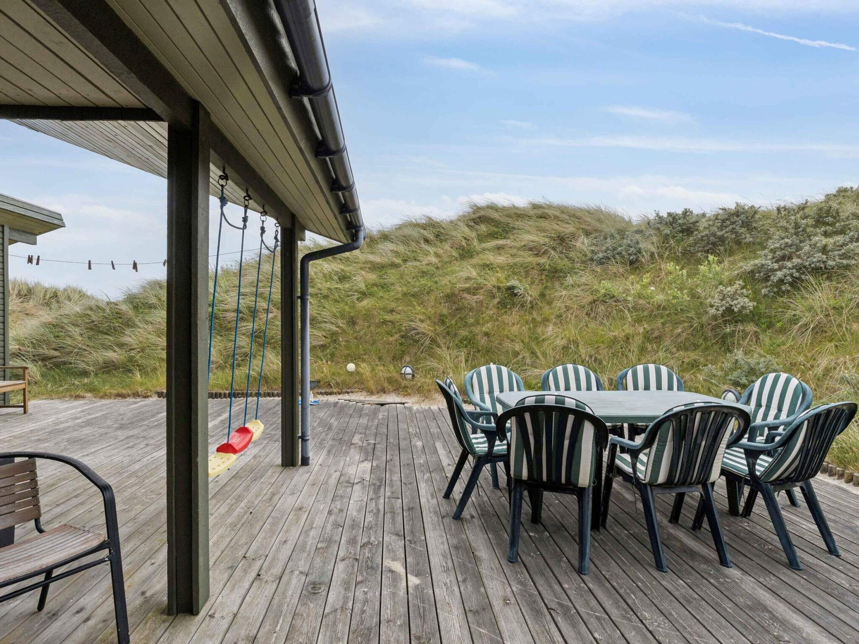 A wooden deck with a table and chairs, overlooking a grassy area with dunes.