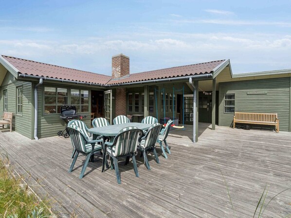 A wooden deck with a dining table and chairs, a grill, and a bench.
