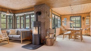 L’intérieur chaleureux d’un chalet comprend un poêle à bois central, un coin repas et un espace détente avec un canapé et des fauteuils.