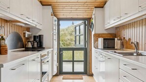 Une cuisine moderne avec des armoires blanches, un plafond en bois et une vue sur la verdure environnante.