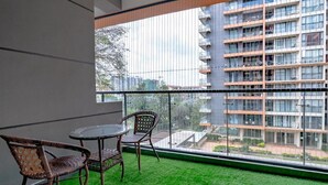 Ein Balkon mit rundem Tisch und Korbstühlen, der auf ein modernes Gebäude mit Balkonen blickt.