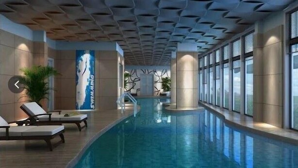 Ein Innenpool mit modernem Deckenbau, Liegestühlen und großen Fenstern.