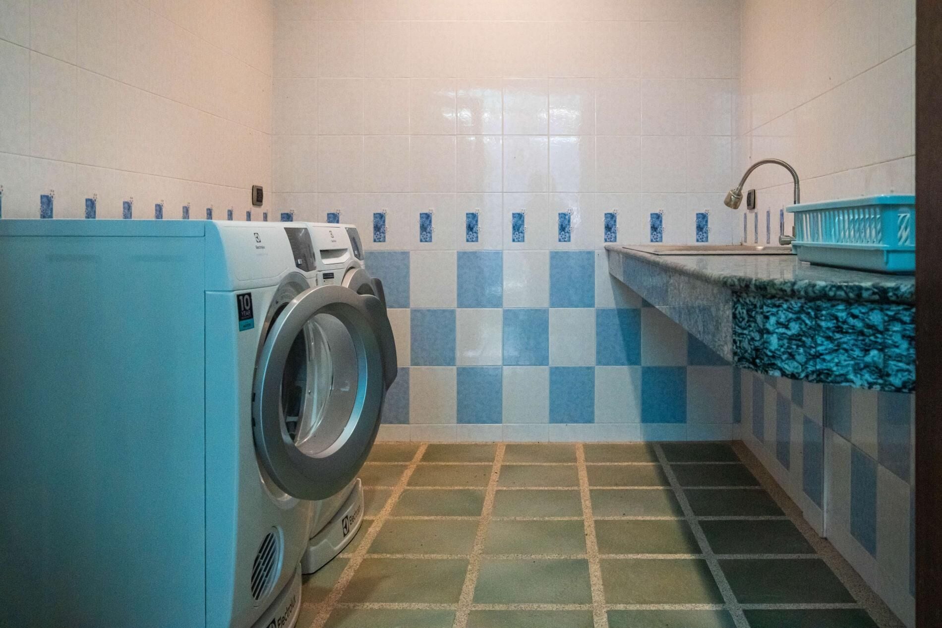A laundry room with a washing machine, a sink, and a tiled floor.