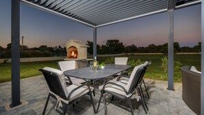 Un patio al aire libre con una mesa redonda y sillas, un brasero y vistas del paisaje circundante.