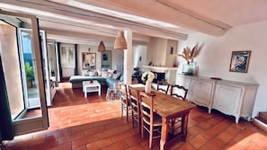 Un vaste espace de vie comprenant une table à manger, des chaises et un canapé. On y trouve également une cheminée et une vue sur l’extérieur grâce à une porte-fenêtre coulissante.