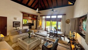 A spacious living area with a high ceiling, a dining set, and a kitchen visible through an open door.