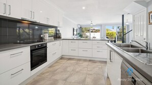 Une cuisine moderne avec des meubles blancs, une cuisinière noire et une grande fenêtre donnant sur un jardin.