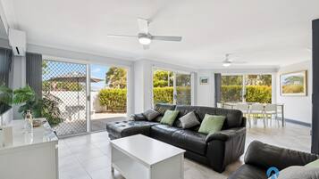 A modern living room with a black leather sofa, a white coffee table, and a dining area with a table and chairs.