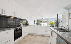 Une cuisine moderne avec des meubles blancs, une cuisinière noire et une grande fenêtre donnant sur un jardin.
