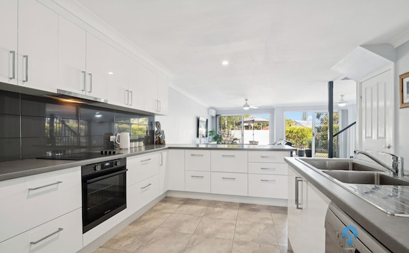 A modern kitchen with white cabinetry, a black stove, and a large window overlooking a garden.