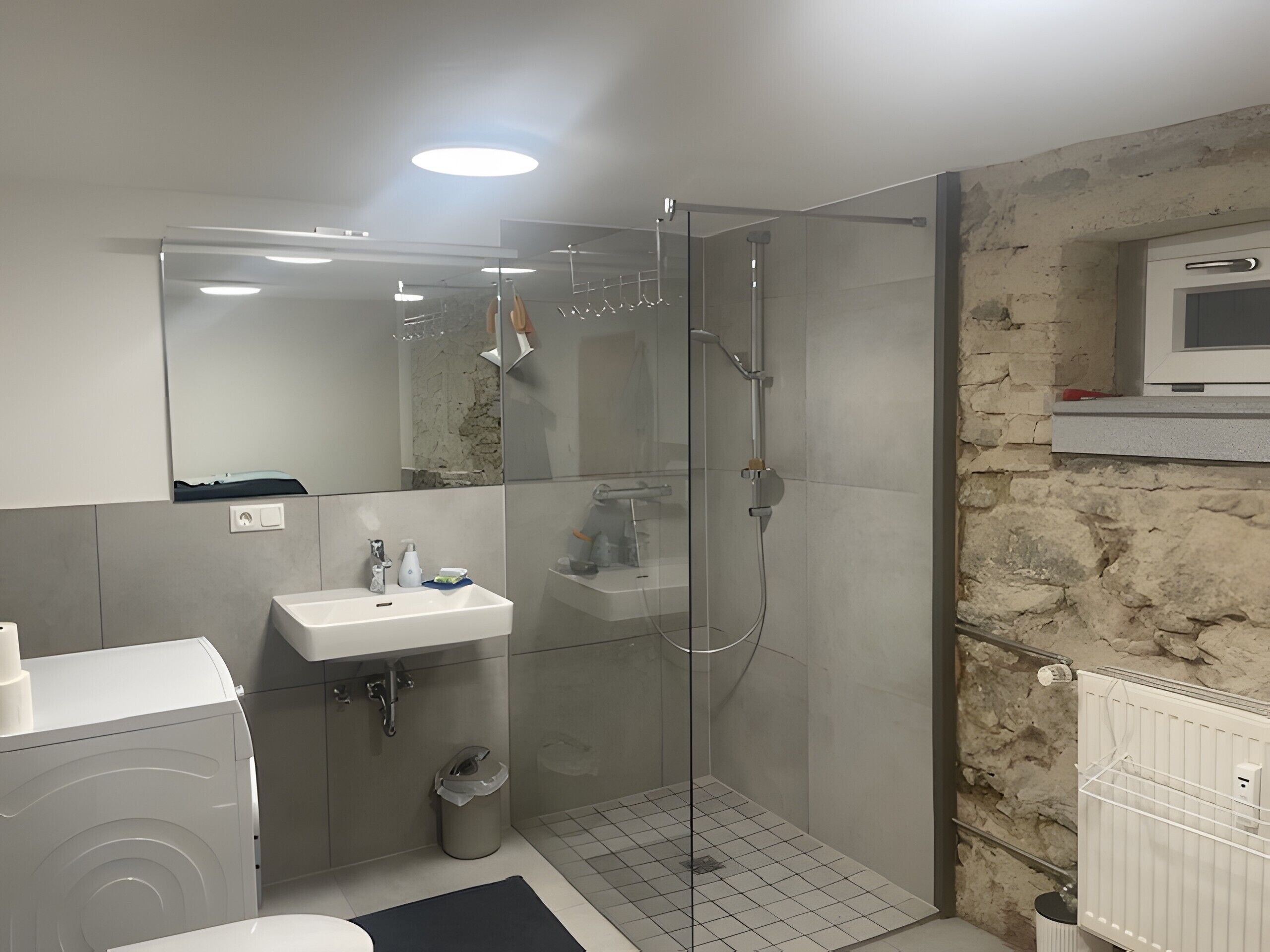A modern bathroom with a glass-enclosed shower, a sink with a mirror above, and a radiator on the wall.