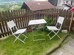 A small outdoor seating area with two white chairs and a table, surrounded by a wooden fence, overlooking a rural landscape. - Apartment 'Gaberlsäge' with Outdoor Seating, Shared Garden, and Wi-Fi (Lam)
