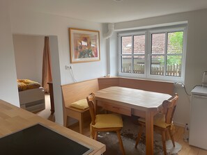 A room with a wooden table and chairs, a window with a view of a fence and greenery, and a painting on the wall. - Apartment 'Gaberlsäge' with Outdoor Seating, Shared Garden, and Wi-Fi (Lam)