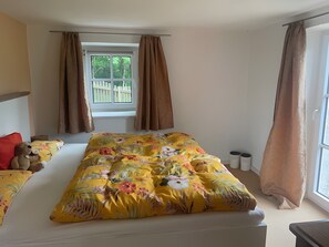 A bedroom with a floral bedspread, a window with curtains, a view of a white fence, and a teddy bear on the bed. - Apartment 'Gaberlsäge' with Outdoor Seating, Shared Garden, and Wi-Fi (Lam)