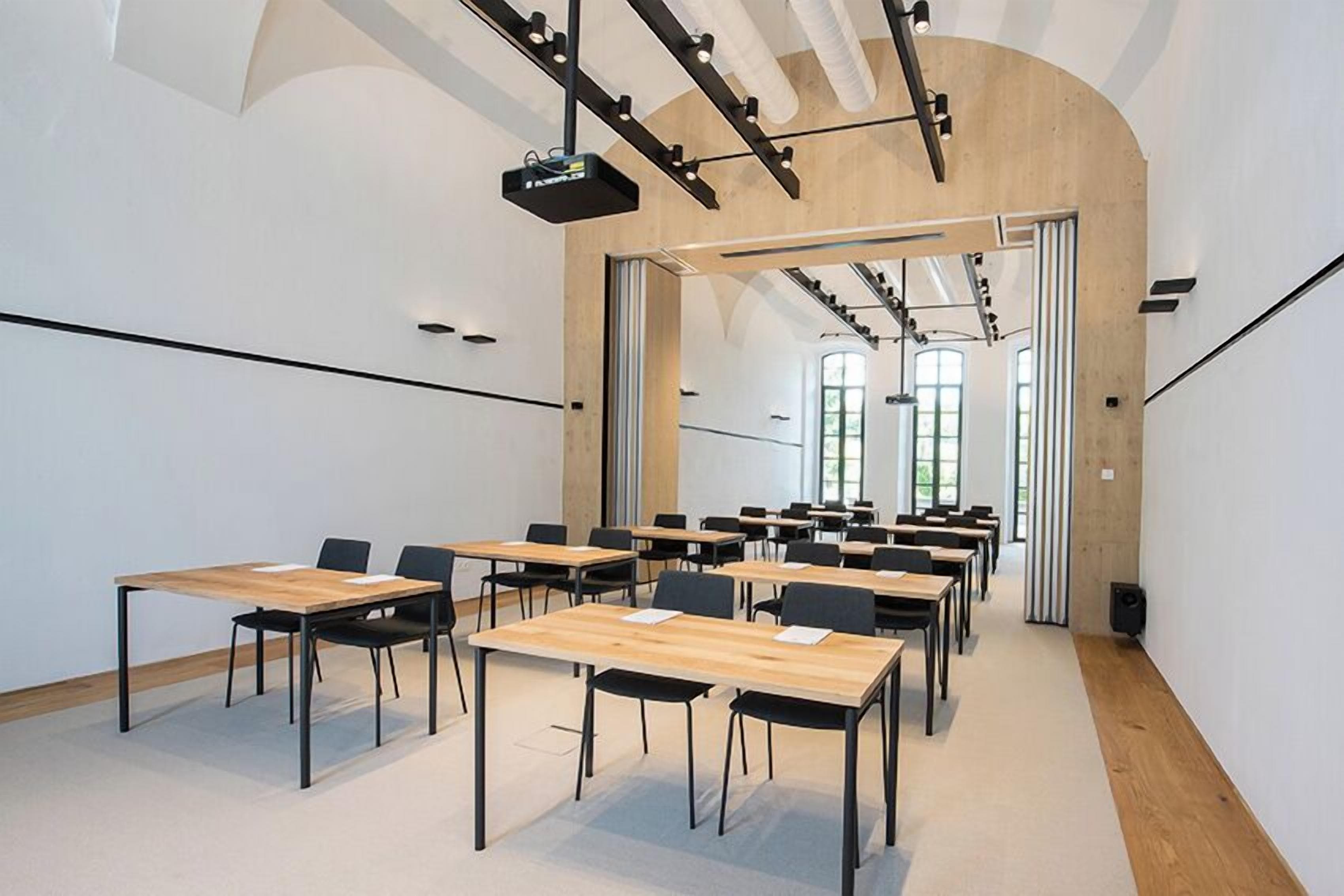 A conference room with multiple tables and chairs, a projector, and a large arched doorway leading to another room.