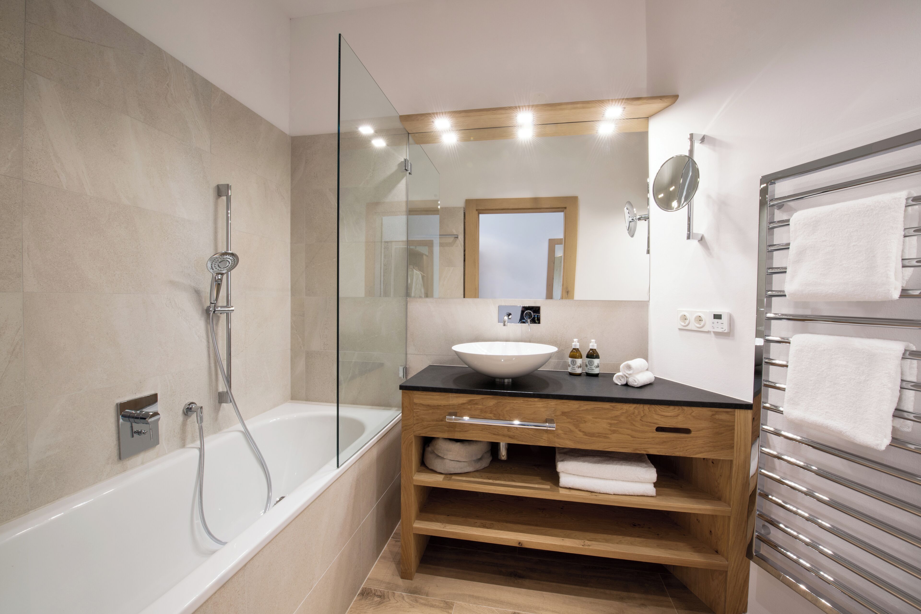 Ein modernes Badezimmer mit einer Duschkabine aus Glas, einem Holzbadezimmermöbel mit Waschbecken und einem Handtuchhalter.