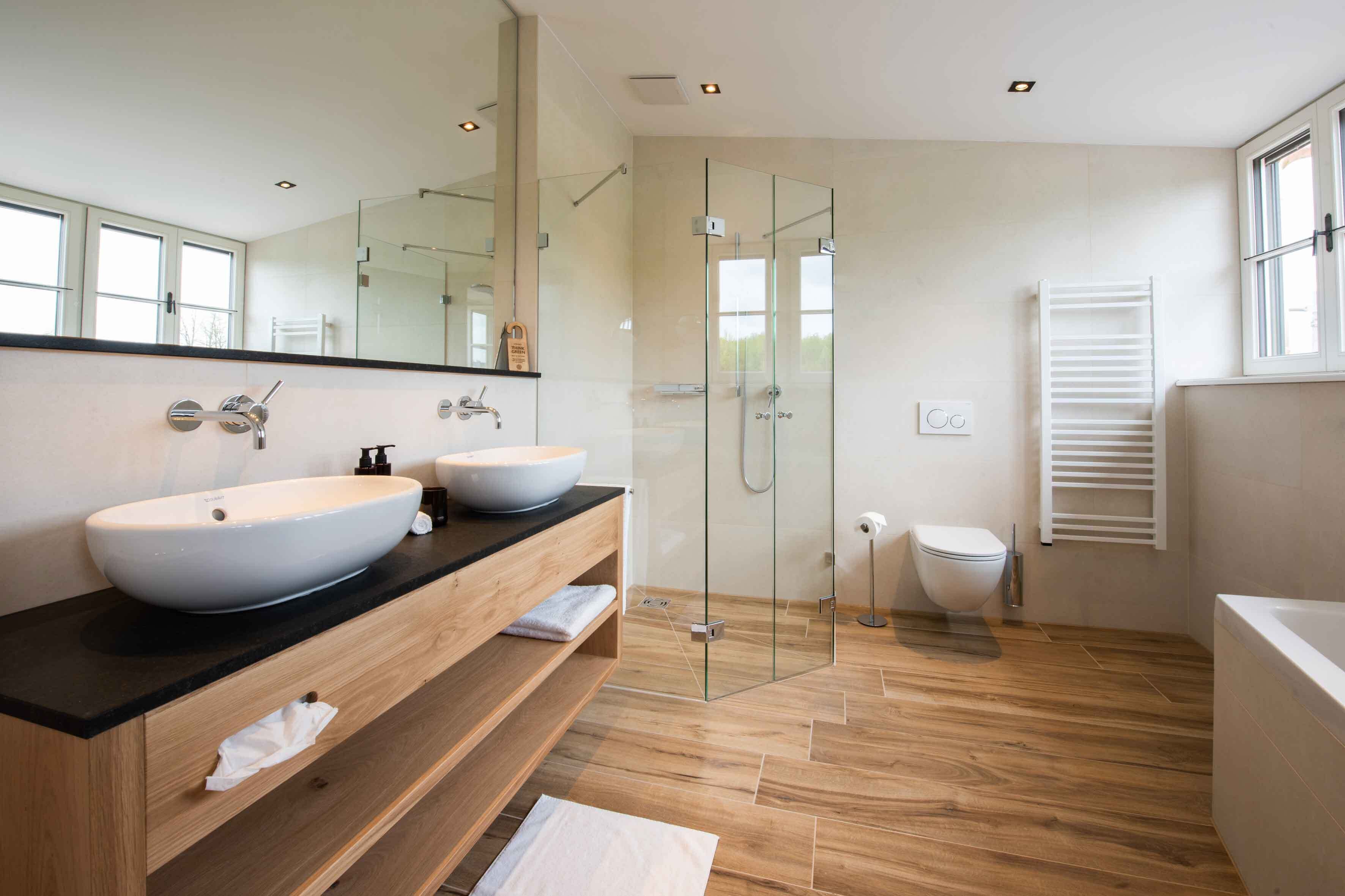 Een moderne badkamer met twee wastafels, een douche met glazen wand, een toilet en een bad.