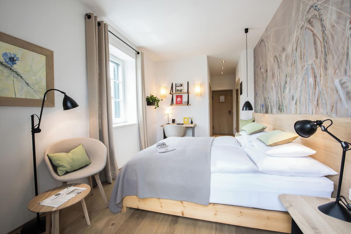Ein modernes Schlafzimmer mit einem hölzernen Bett, einem Sessel, einem Schreibtisch und einem großen Fenster.