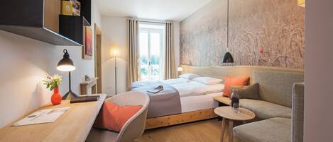 A modern hotel room with a bed, a desk, a chair, a sofa, and a large window.