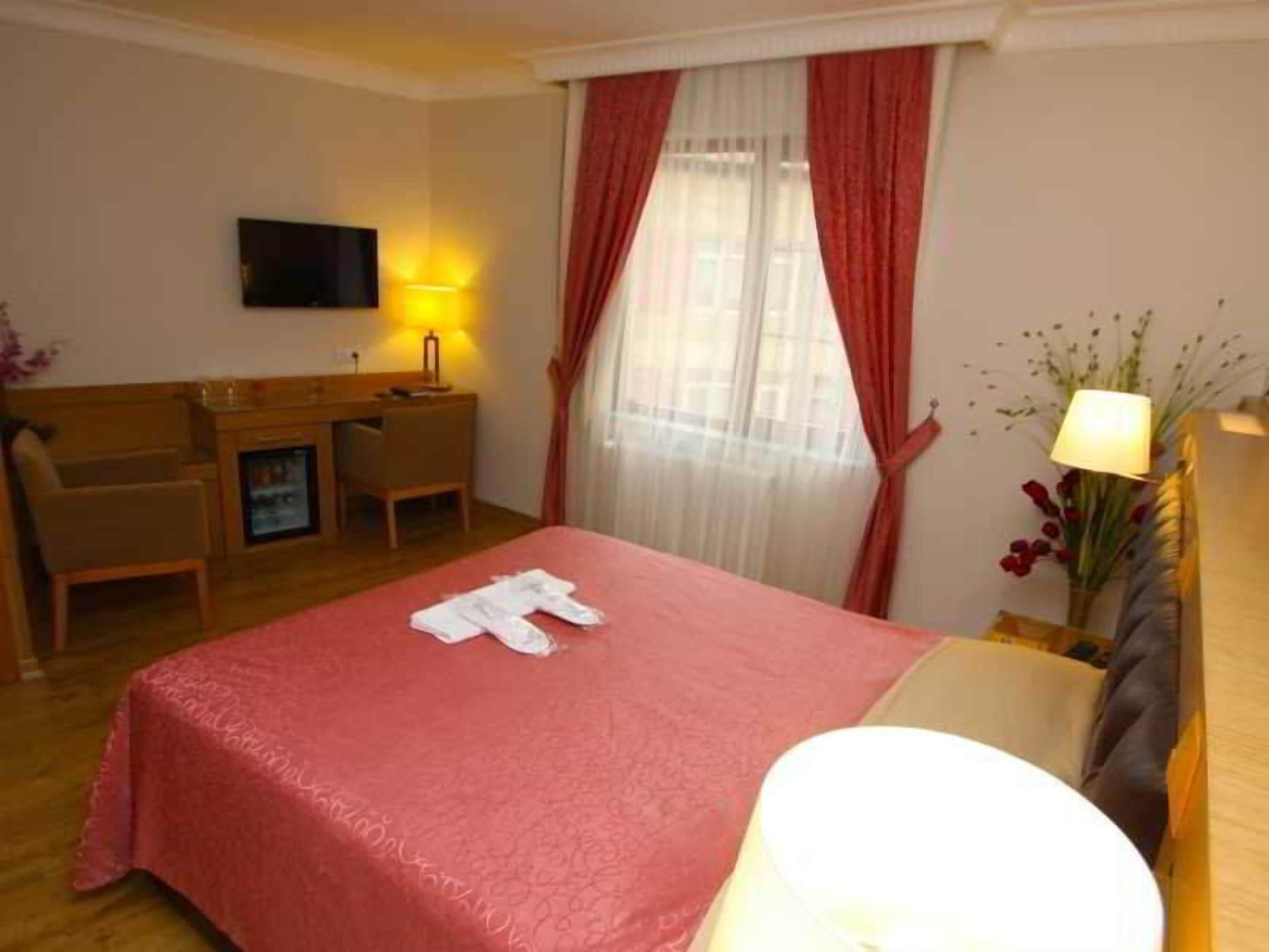 Ein Hotelzimmer mit Bett, Schreibtisch, Stuhl, Fernseher und einem Fenster mit Vorhängen.