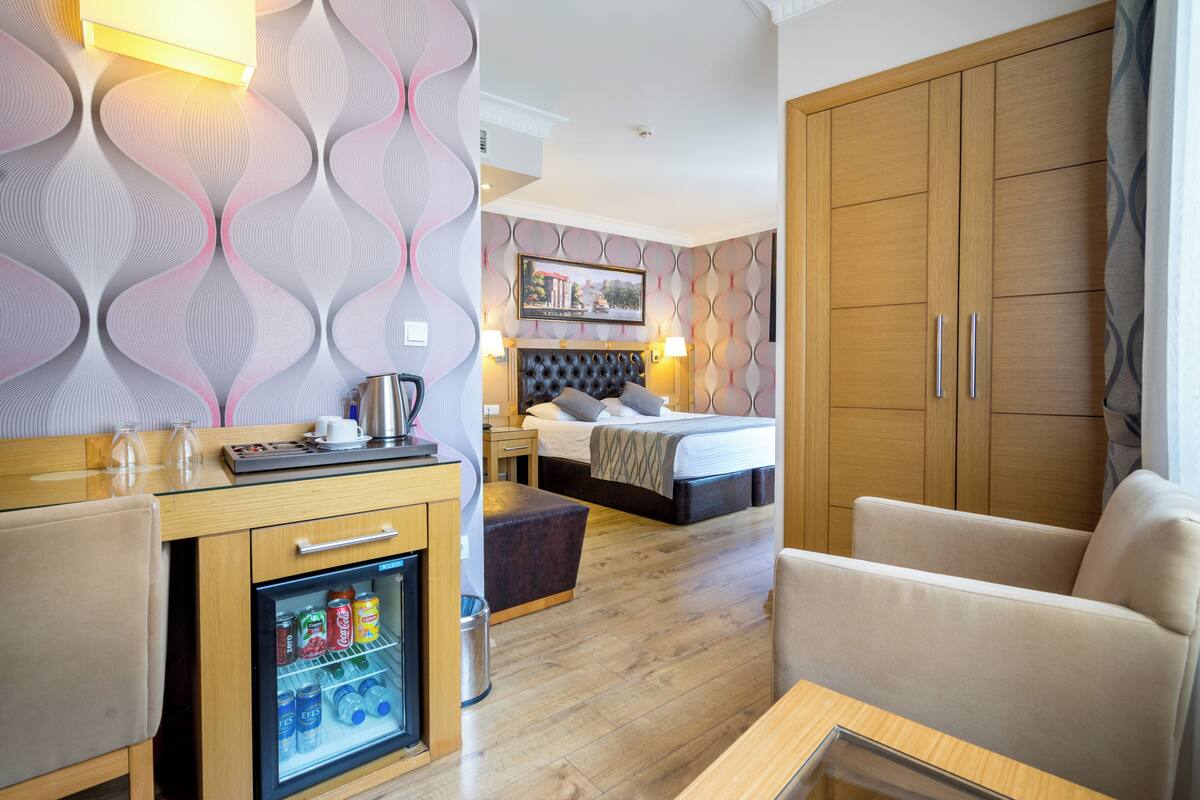 A hotel room with a bed, a desk with a refrigerator, a sofa, and a wardrobe.