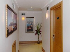 A hallway with a framed picture on the left, a framed picture on the right, and a vase with flowers in the center. - Levent Hotel Istanbul (Istanbul)
